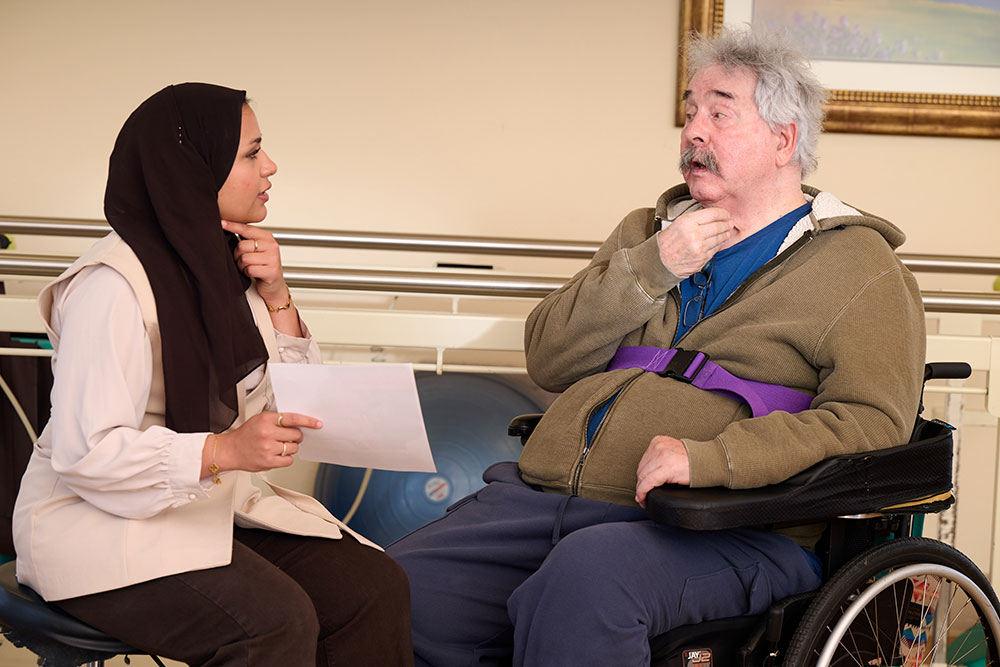 Image of a speech-language pathologist talking with a patient across a desk.